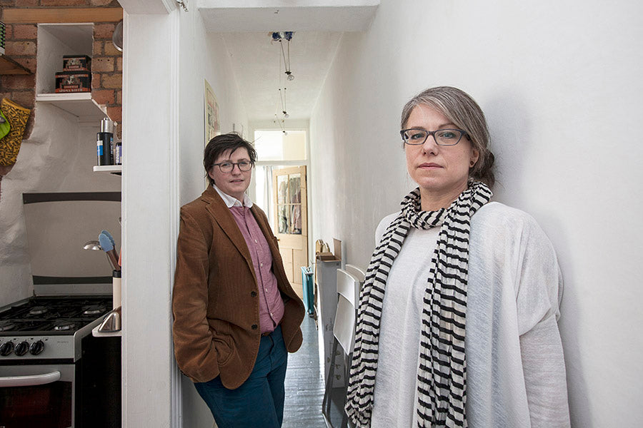 Two people standing in a narrow hallway with a kitchen on one side.