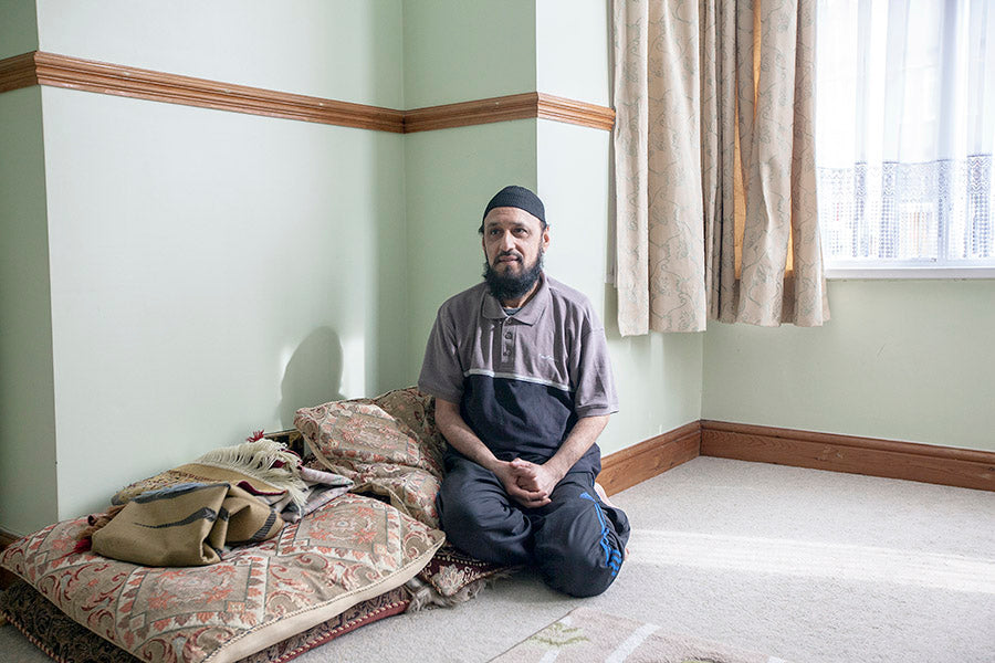 Man sitting on a bed in a room with light green walls and a window.