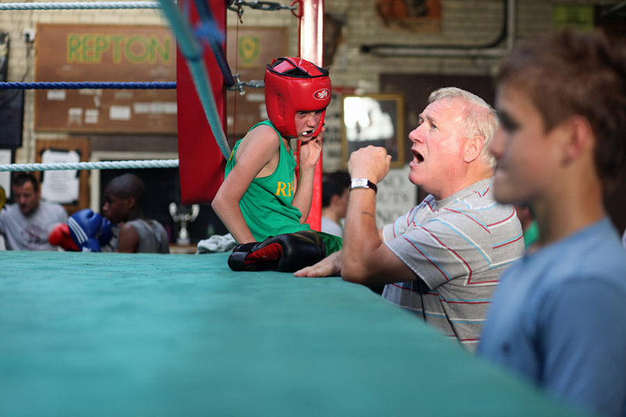 Person in a boxing ring with a coach and spectators in the background