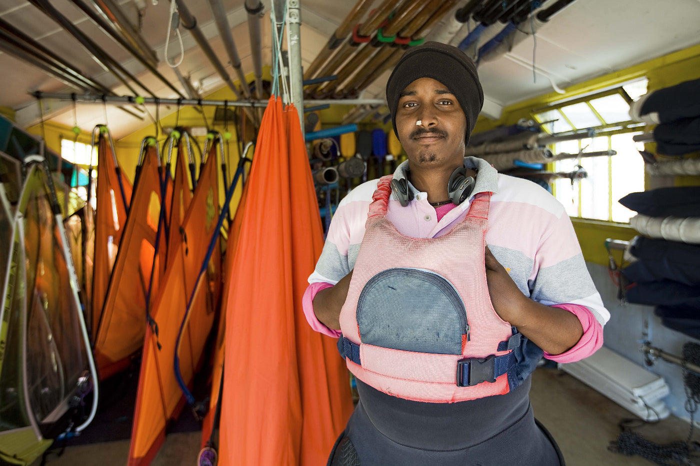 Person wearing a pink life jacket in a storage room with kayaks and equipment.
