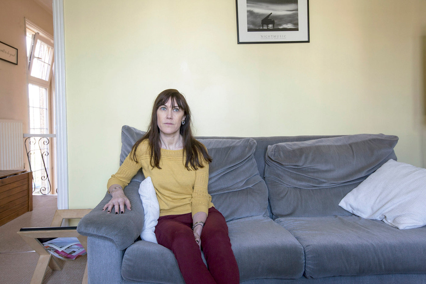 Woman sitting on a gray sofa in a living room with a neutral color scheme.