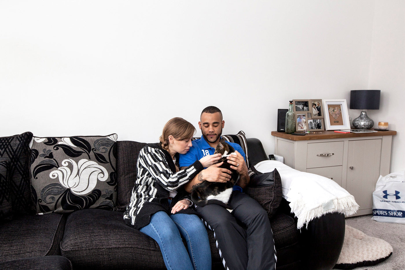 Two people sitting on a couch in a living room, one holding a cat.