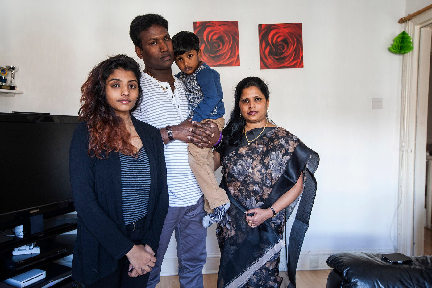 Family of four standing together in a living room with red abstract art on the wall.