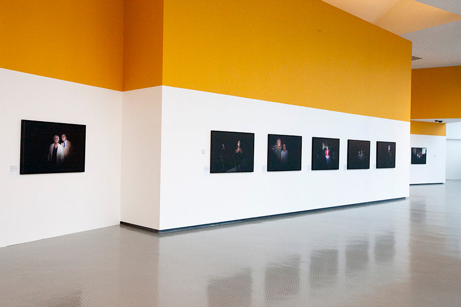 Art gallery with yellow walls and a row of framed artworks on a white wall.
