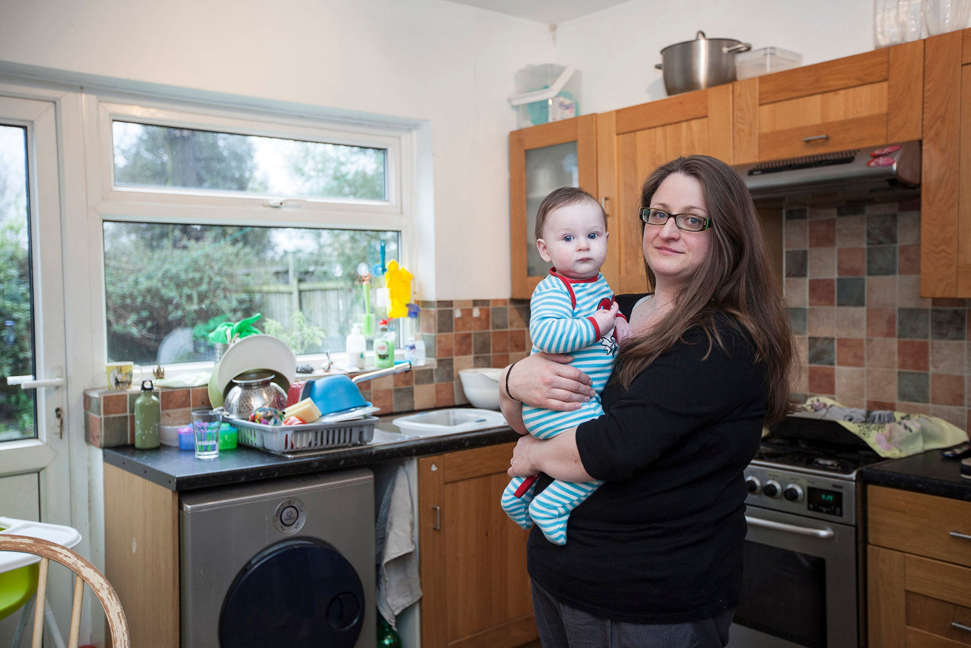 Woman holding a baby in a kitchen with appliances and cabinets.