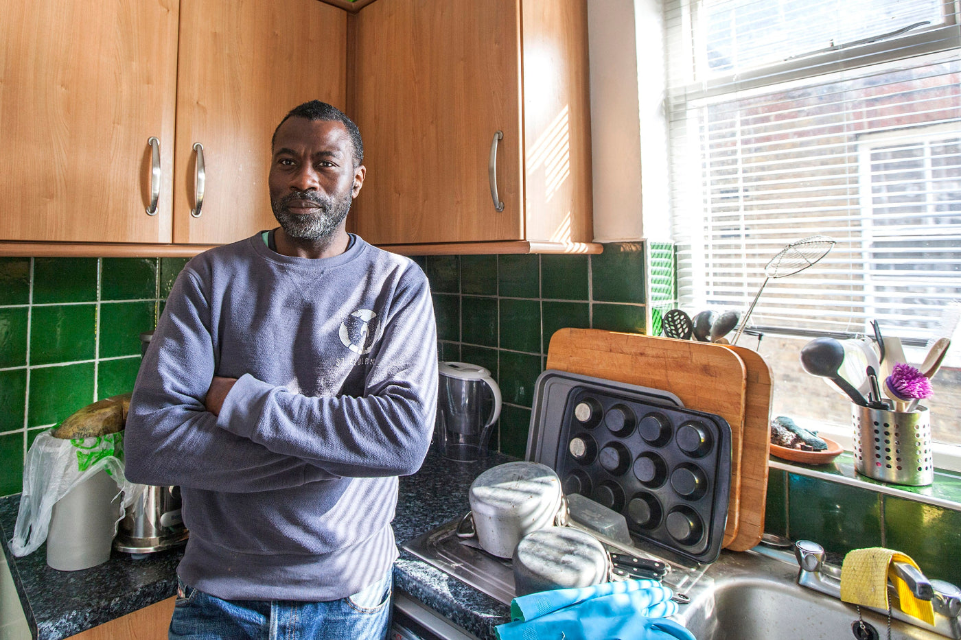 Man standing in a kitchen with green tiled walls and wooden cabinets.