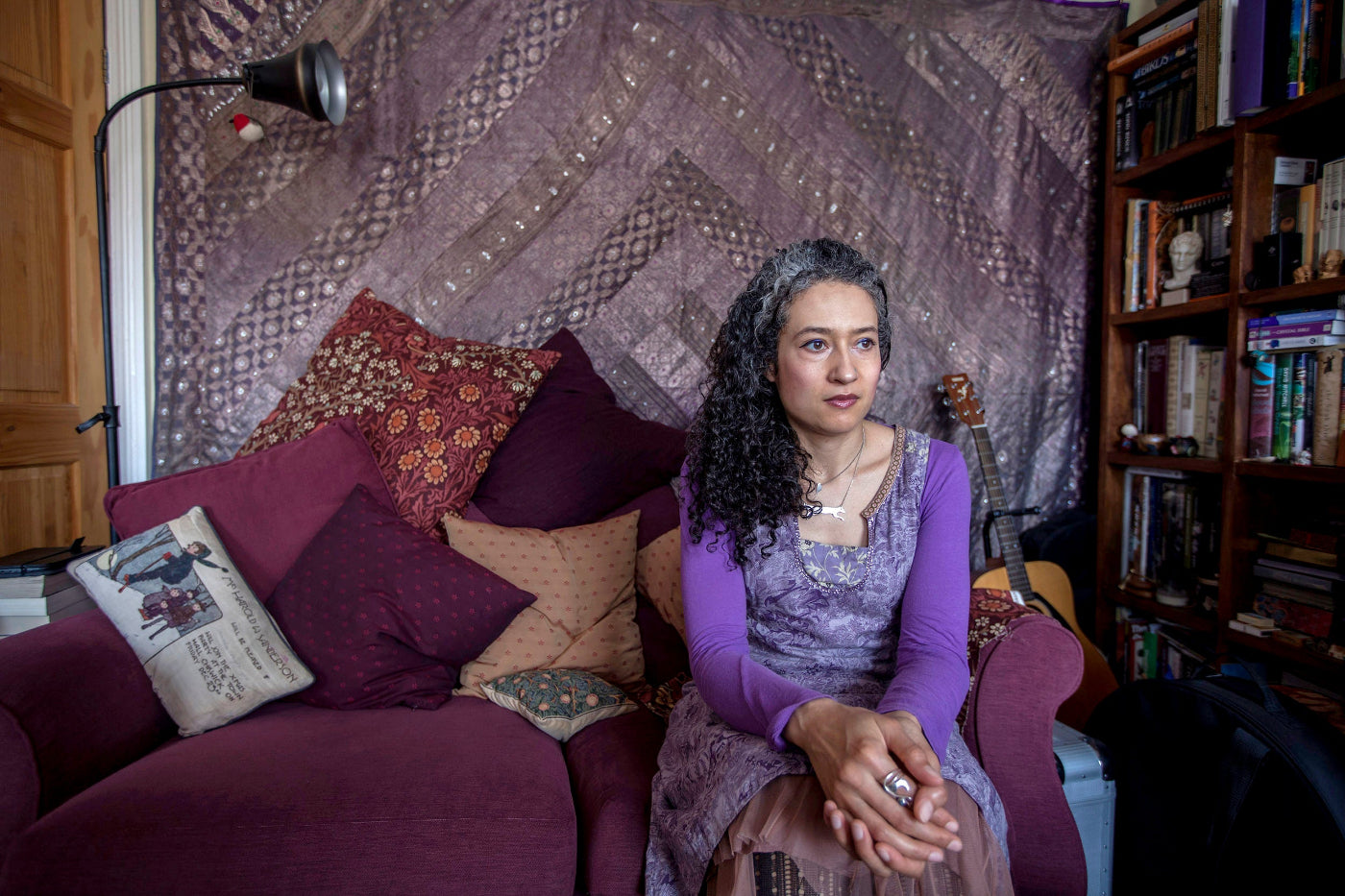 Woman sitting on a couch in a room with books and decorative pillows.