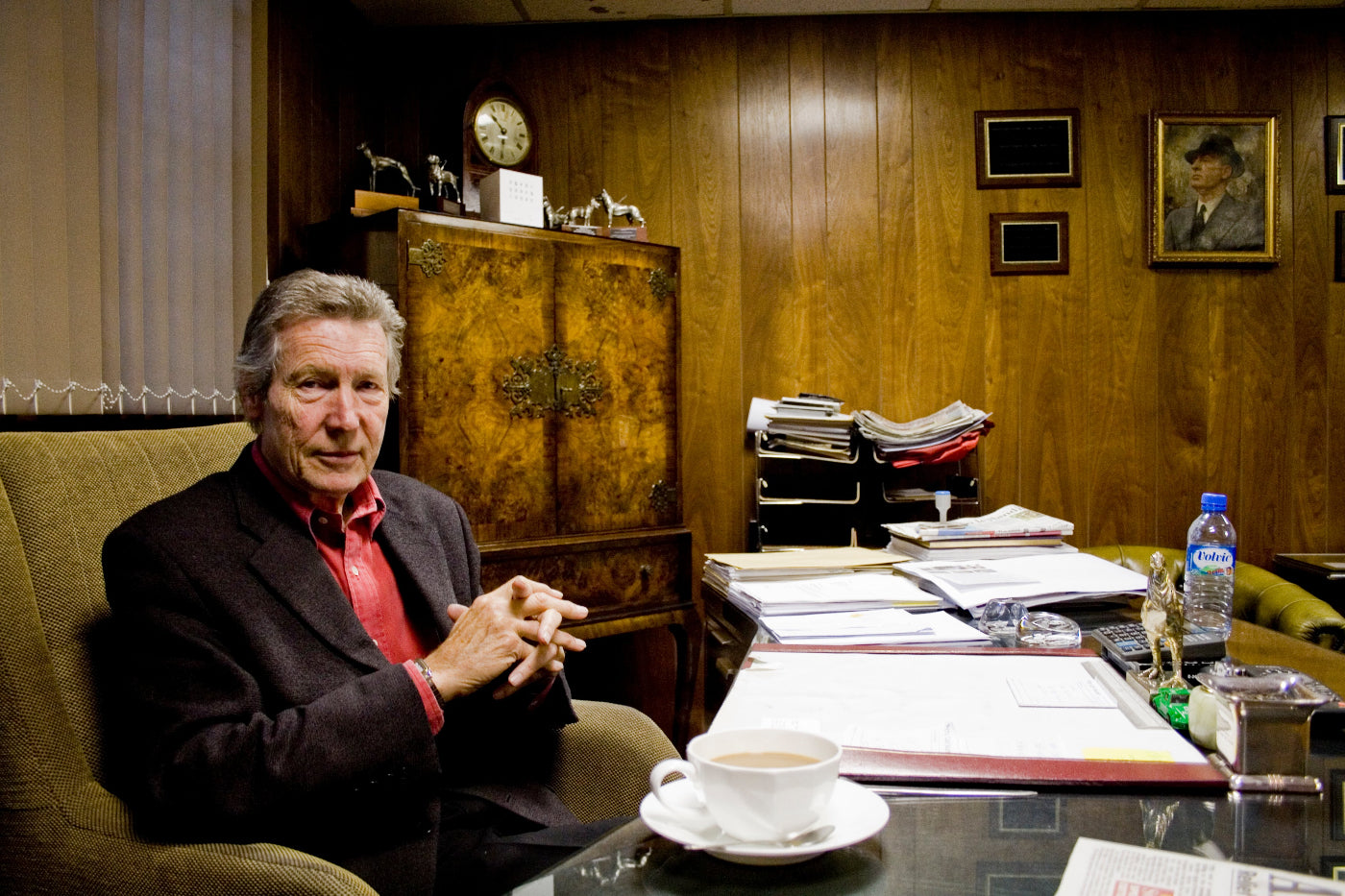 Man sitting at a desk in a wood panelled office with a cup of coffee and documents.