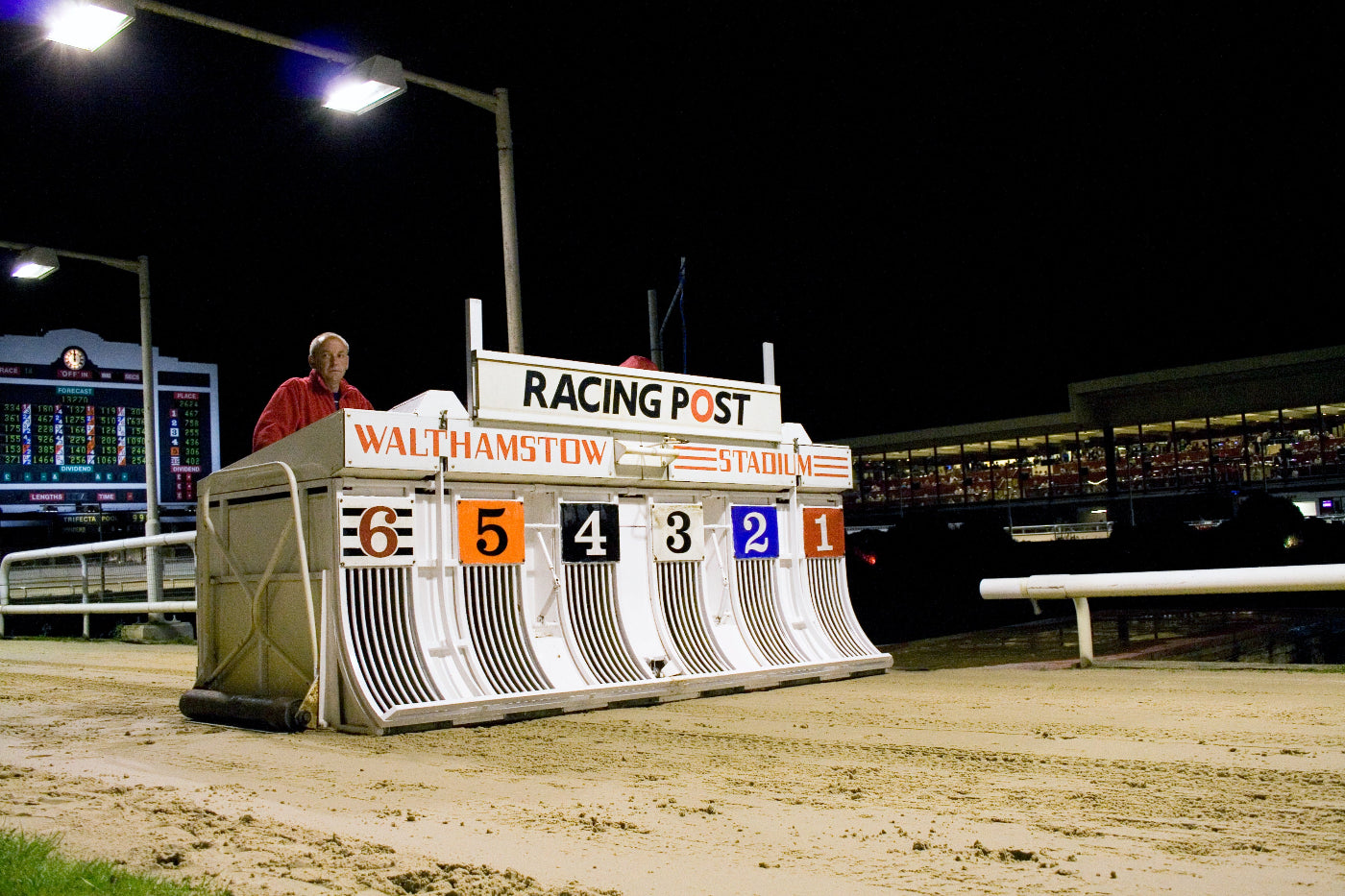 Dog racing starting gate with 'Racing Post' branding at Walthamstow Stadium at night.