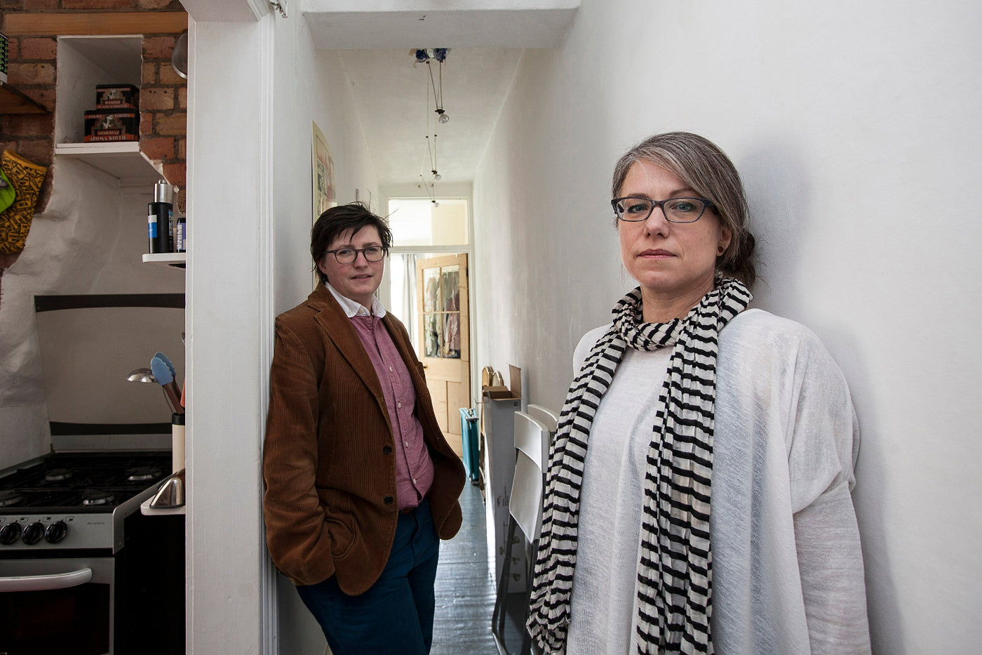 Two people standing in a kitchen and hallway.
