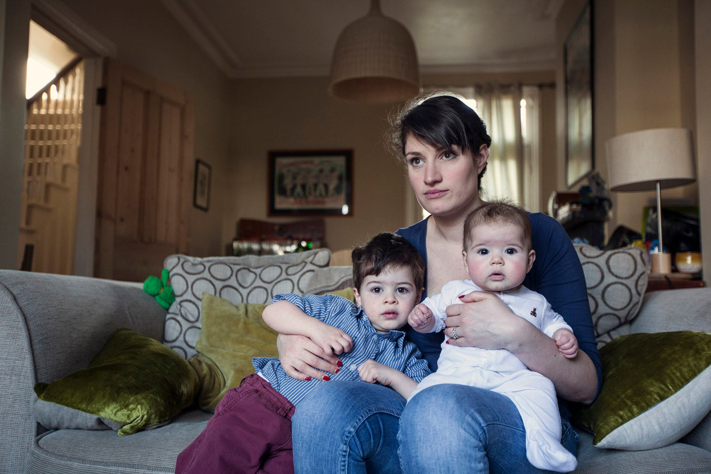 Woman sitting on a couch holding two children in a living room.