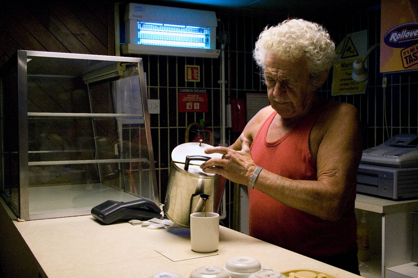 Person pouring a large pot of tea in a kitchen setting with various appliances and equipment.