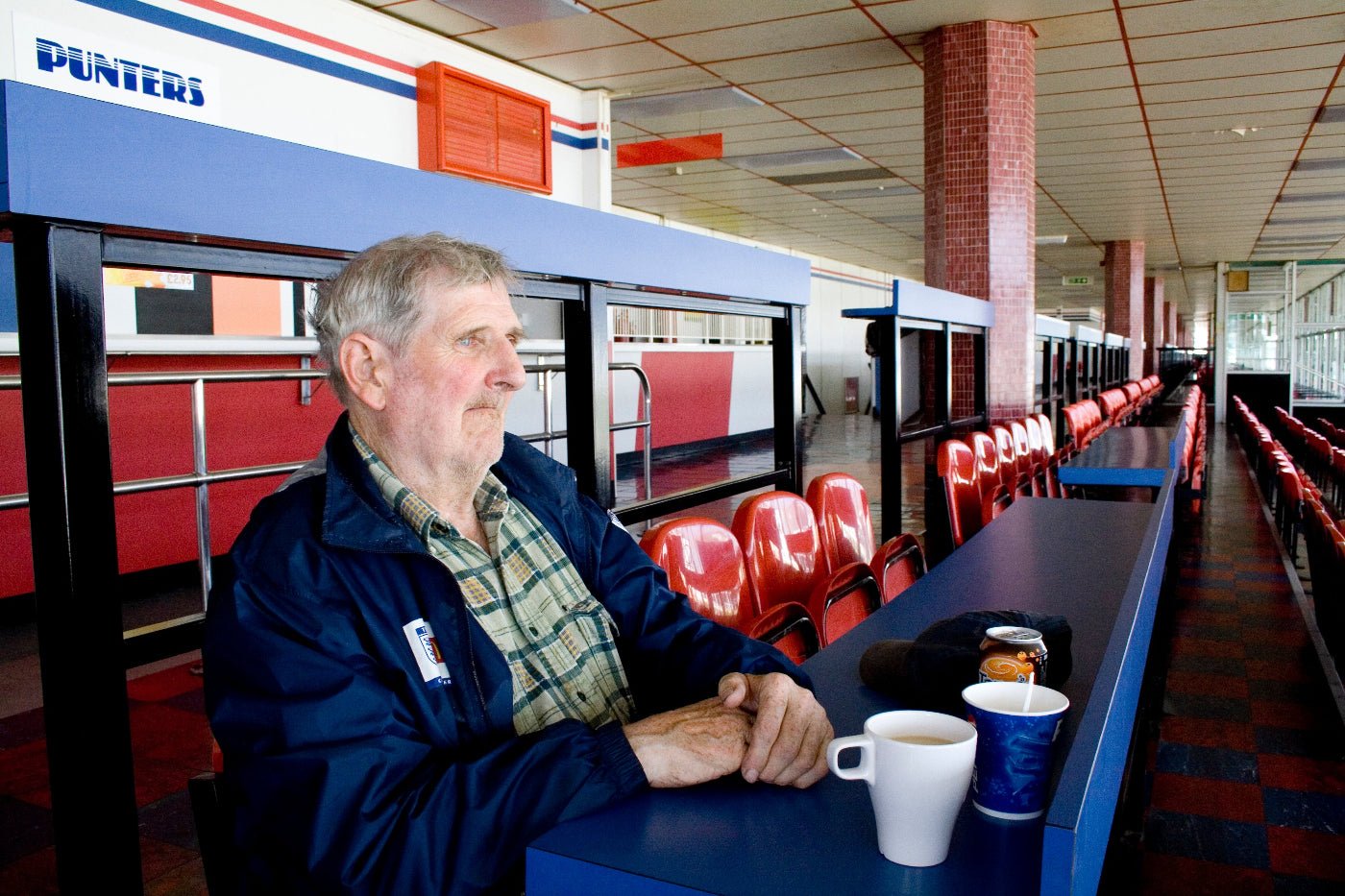 Man sitting at a table with a cup and a blue mug at the race track.