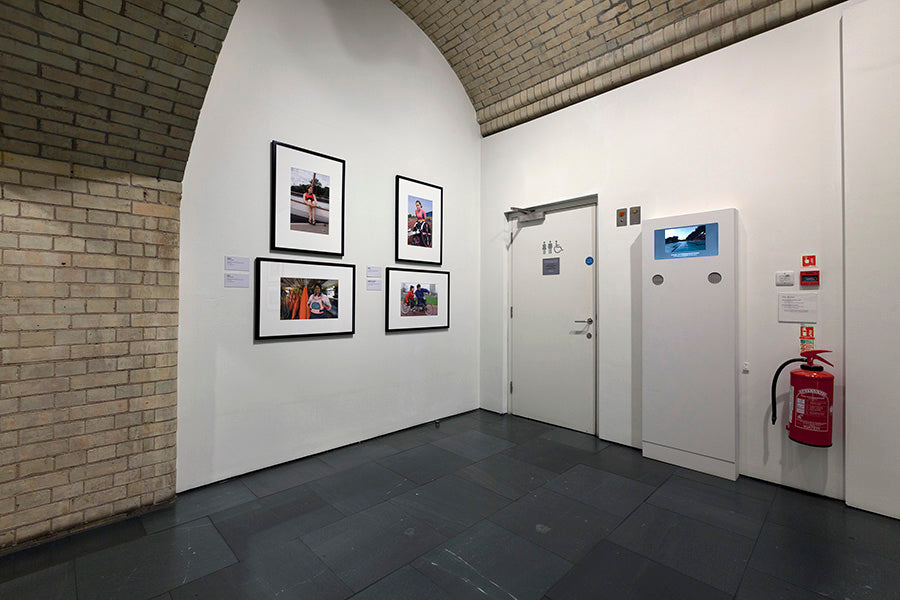 Art gallery with framed photographs on a white wall, a door, and a fire extinguisher.