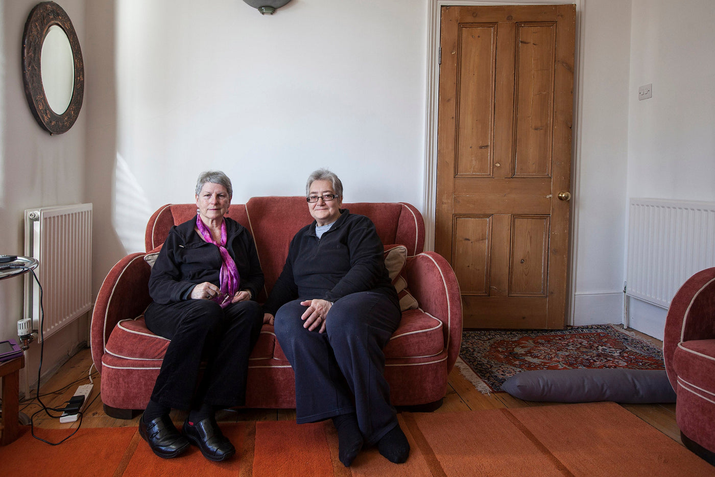 Two older women sitting on a red sofa in a living room.