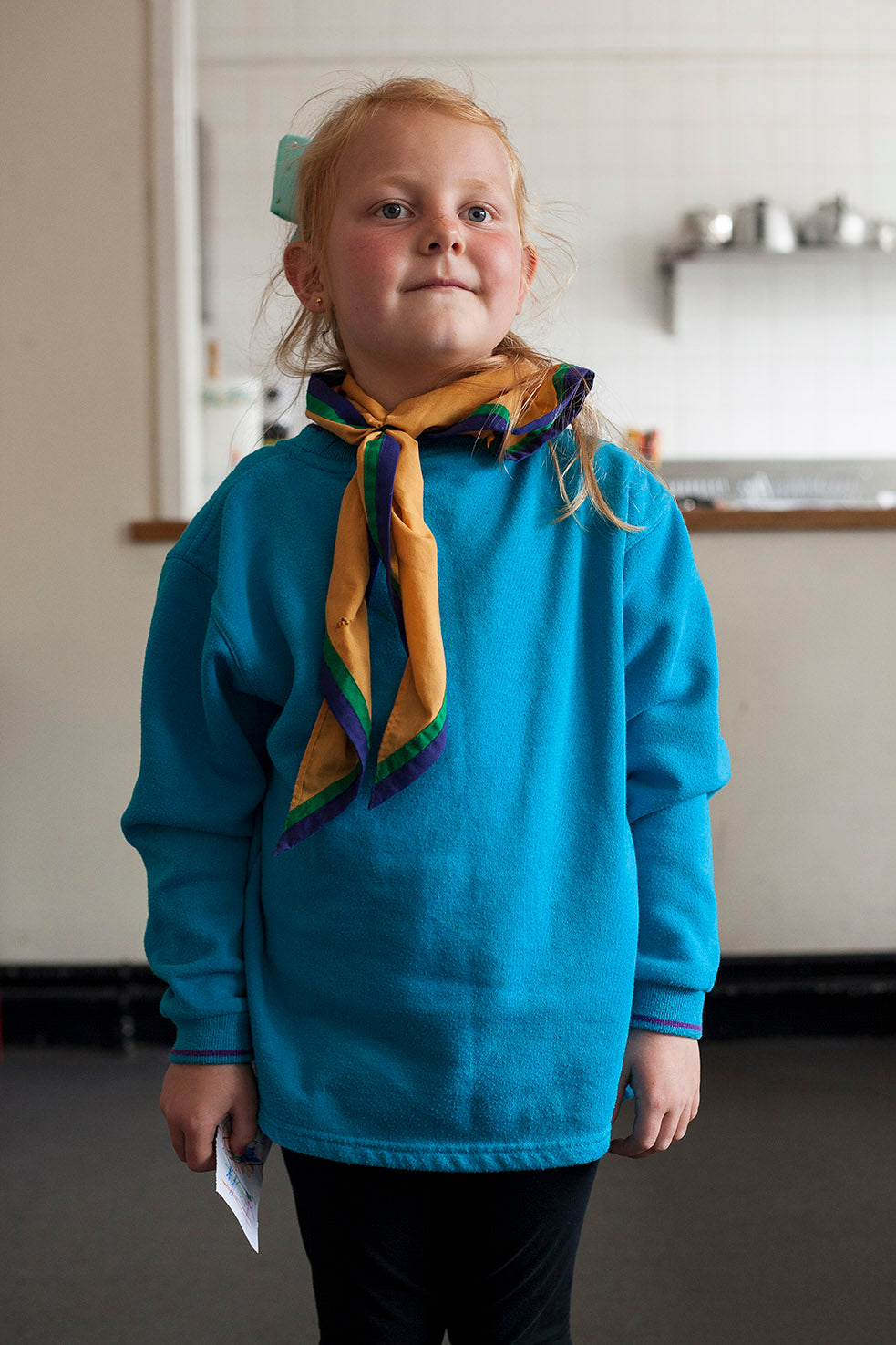Young girl wearing a blue sweater and colorful scarf indoors