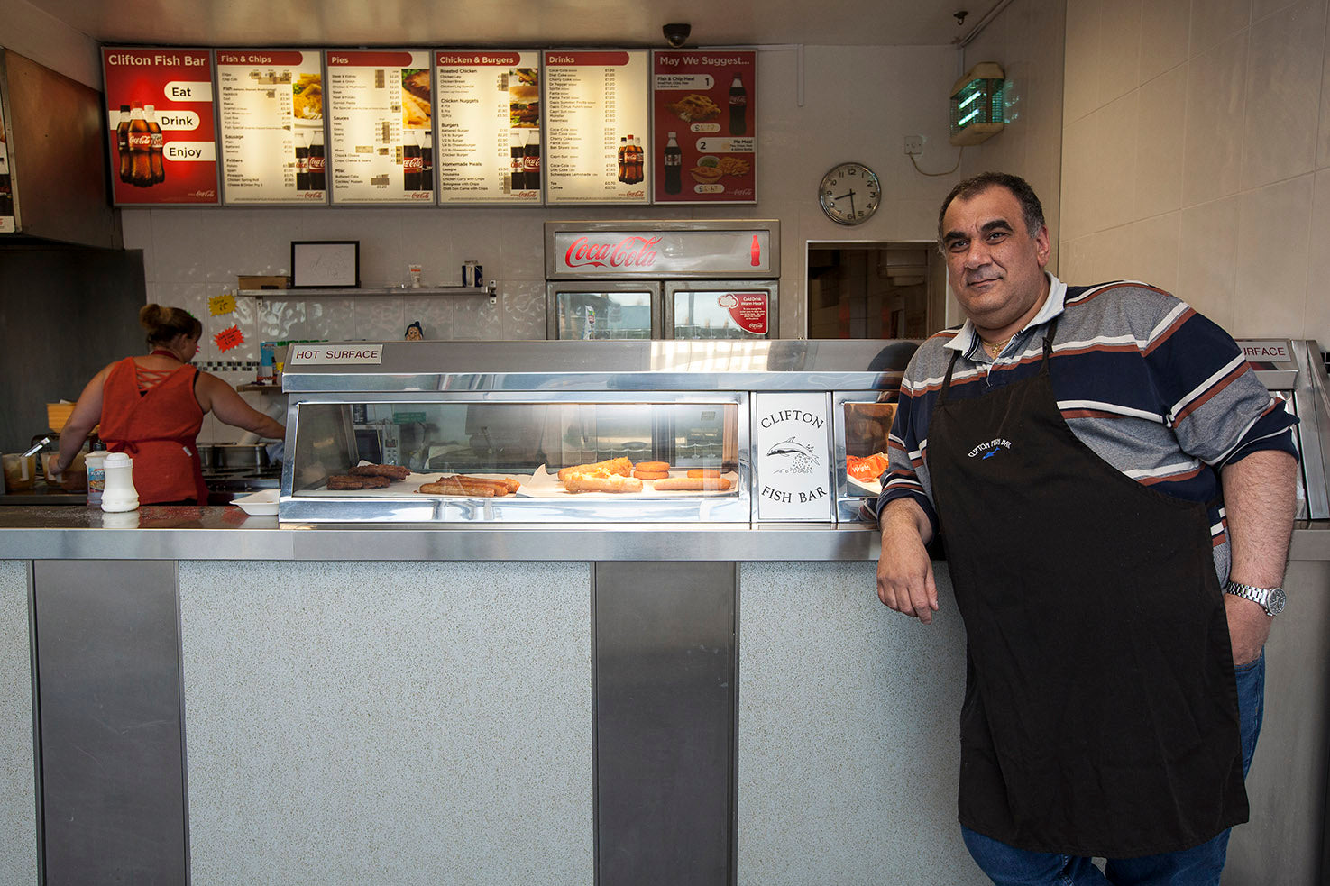 Man standing behind a counter in a fast food restaurant with menu boards on the wall.