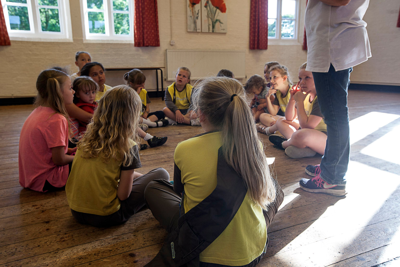 Children sitting on the floor in a classroom setting with a teacher.